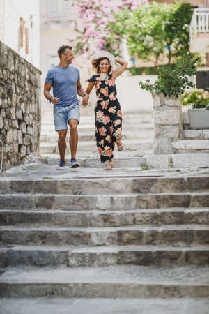 Cheerful couple in love having fun and enjoying summer vacation while running down the stairs in the...