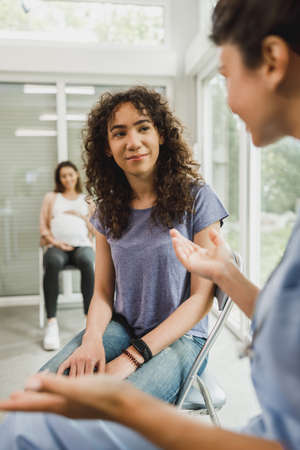 Upset African American teenage girl talks with nurse while waits for gynecologist check up.の写真素材