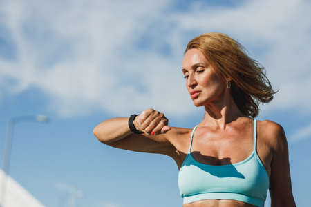 Portrait of a middle age fit woman looking on smartwatch and resting after hard training outdoor.の写真素材