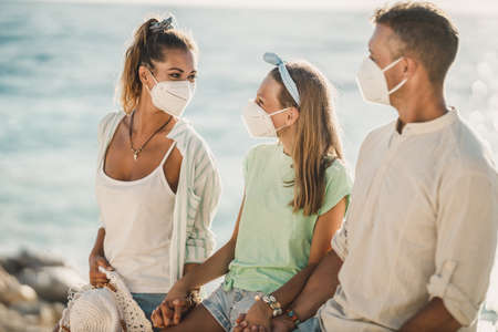 Happy family with protective N95 mask having self-isolation on the seaside at pandemic.