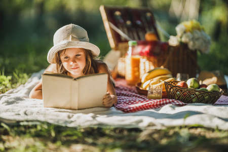 A cute little girl reading a book while enjoying picnic day in nature.の写真素材