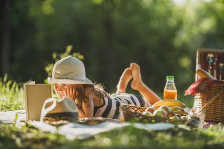 A cute little girl reading a book while enjoying picnic day in nature.の写真素材