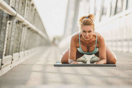 Middle age sportswoman warming up and stretching her body on a bridge. Looking at camera.の写真素材