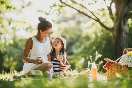 Beautiful mother and her cute daughter drinking orange juice in the park and enjoying a picnic day.の写真素材