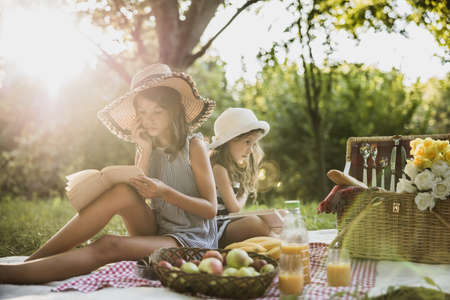 Two cute sisters reading books in nature and enjoying a picnic day.の写真素材