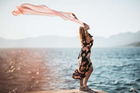 An attractive young woman in flower dress with scarf is having fun and enjoying a summer vacation on the seacost.の写真素材
