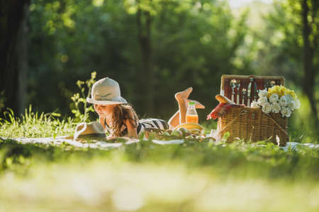 A cute little girl lying on the blanket on a grass and spending a spring day on picnic.の写真素材