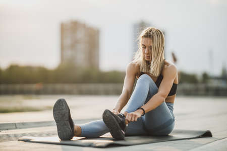 A sporty young woman tying her shoelaces while exercising outdoors.の写真素材