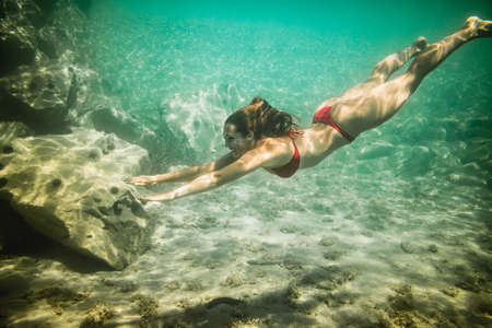 A beautiful young woman is having fun at summer vacation exploring seafloor during scuba diving in sea.の写真素材