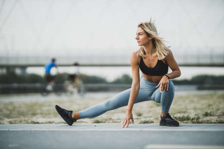 A sporty young woman warming up and stretching her leg while exercising outdoors.の写真素材