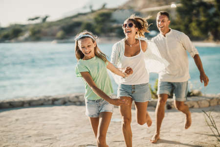 A smiling teenage girl and her parents walking near the sea while having fun at summer vacation.の写真素材