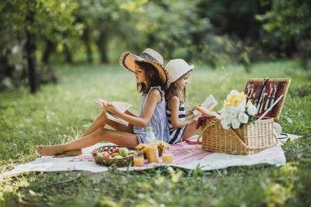 Two cute sisters reading books in nature and enjoying a picnic day.の写真素材