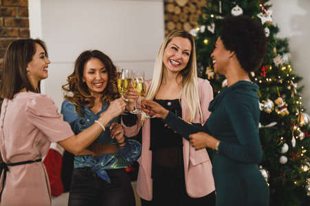 Cheerful multietnic girls having fun while toasting with champagne on Christmas or New Year's home party together.の写真素材