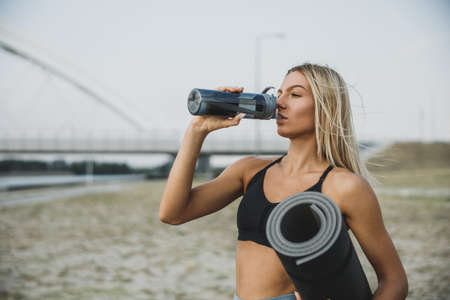 Beautiful fit woman drinking water and resting after training near to river bridge in the city.の写真素材