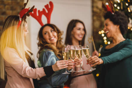 Cheerful multietnic girls toasting with champagne on Christmas or New Year's party. Close-up on the wine glasses.の写真素材