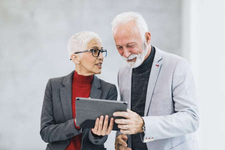 A successful mature businesswoman and her senior colleague using app on a digital tablet while walking in the office hall.の写真素材