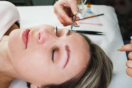 Close up of an unrecognizable beautician doing eyebrow lamination procedure to beautiful mature woman.の写真素材