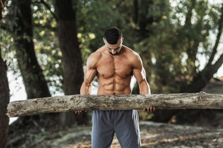 Muscular young man with naked torso doing exercises with timber in the nature.の写真素材