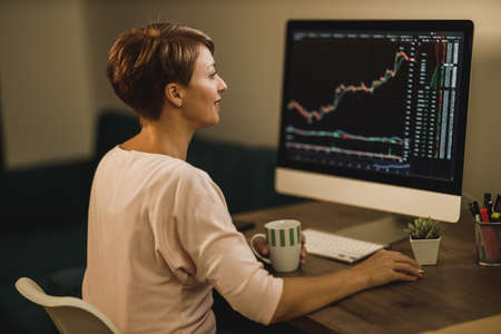 Middle age woman is enjoying her success. She is reading good news on a computer while trading with...