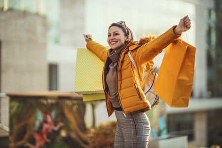 A young happy smiling woman is walking along the street of a city with shopping bags.の写真素材