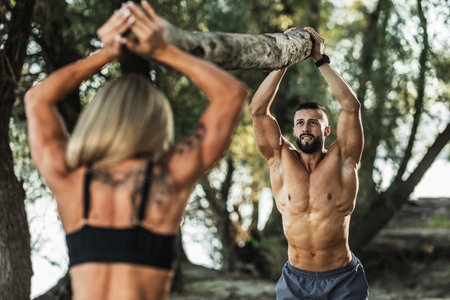 Fitness instructor with muscular female client doing hard training with timber outdoors.