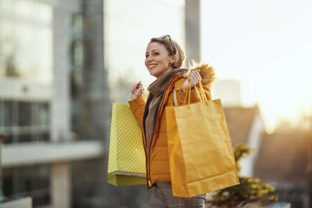 A young happy smiling woman is walking along the street of a city with shopping bags.の写真素材