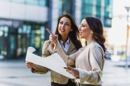 Two attractive smiling businesswoman engineer chatting and looking over plans outside an office.の写真素材