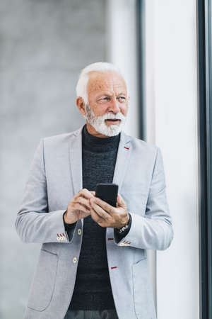 A confident senior businessman using app on smart phone while standing in the office.
