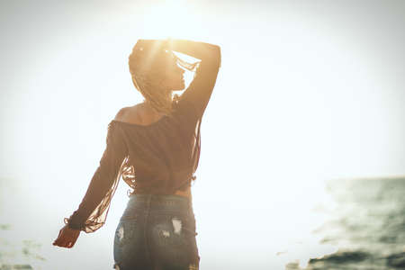 A beautiful young woman is relaxing on the beach.  She is posing and looking at the sunset.