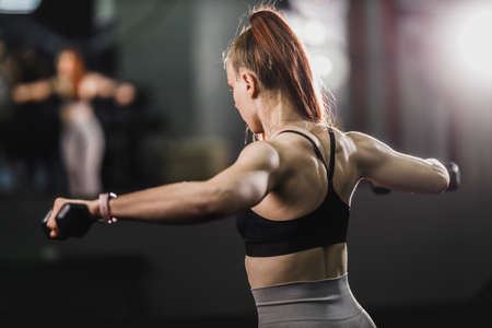 Shot of a muscular young woman in sportswear working out at the hard training in the gym. She is pumping up shoulder muscule with heavy weight.の写真素材