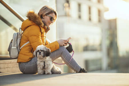 Beautiful young fashion woman is spending time with her cute pet dog playing in the city street...