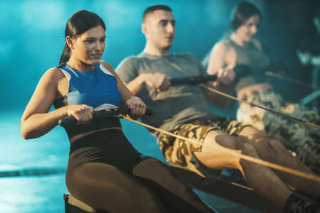 Three young muscular friends are having hard workout. They are pulling the row machine in the gym.の写真素材
