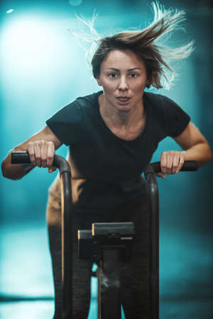 A young muscular woman is doing hard cal bike crossfit training in the gym.の写真素材