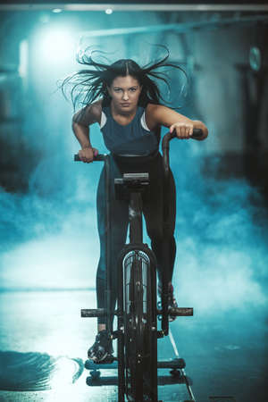 A young muscular woman is doing hard cal bike crossfit training in the gym.の写真素材