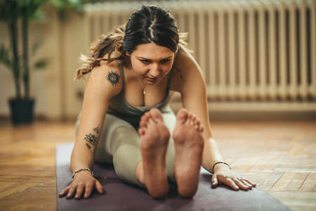 Young woman is doing yoga meditation in the living room at home. She is meditating on floor mat in morning sunshine.の写真素材