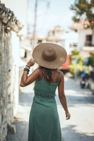 A beautiful smiling young woman with straw hat is walking along the streets of a Mediterranean town and enjoys in summer sunny day.の写真素材