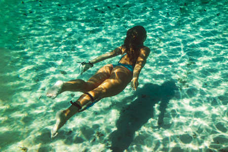 A beautiful young woman is having fun at summer vacation exploring seafloor during scuba diving in...