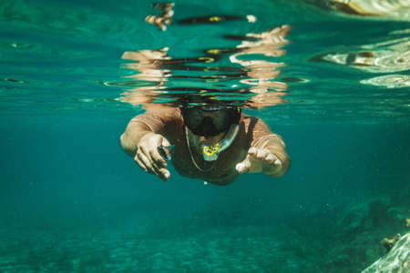 A handsome man is having fun at summer vacation and exploring seafloor during scuba diving in sea.の写真素材