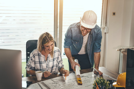 Two young pensive architect colleagues are working on a new project, analyzing blueprints and talking about it in the office.の写真素材