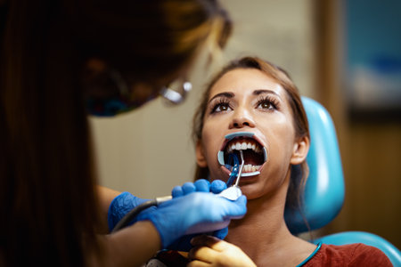The beautiful young woman is at the dentist. She sits in the dentist's chair and the dentist sets braces on her teeth putting aesthetic self-aligning lingual locks.の写真素材