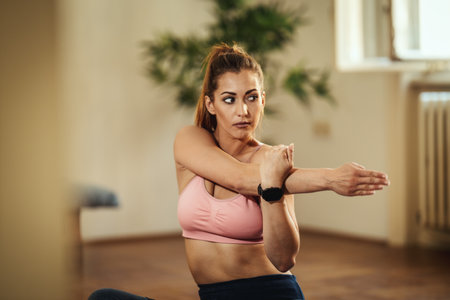 Young smiling woman is doing stretching exercises at home in morning sunshine.の写真素材