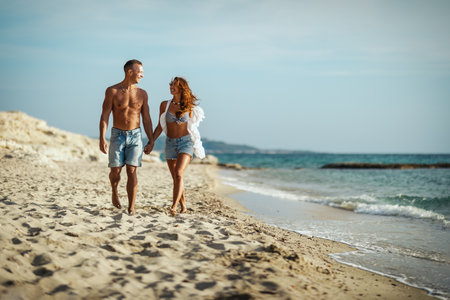 A loving couple is having fun and walking on the empty sandy sea beach.They are looking each other and happily smiling.の写真素材