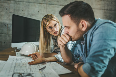 Two young pensive architect colleagues are working on a new project, analyzing blueprints and talking about it in the office.の写真素材