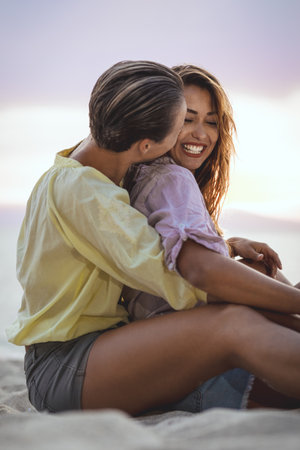 Happy female gay couple are enjoying in summer day on the sea beach. They are hugging and looking...