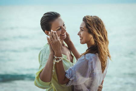 Two young happy women are enjoying in summer day. They are hugging and looking each other with smile.の写真素材
