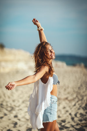 A beautiful young woman is relaxing on the beach with raised arms.の写真素材