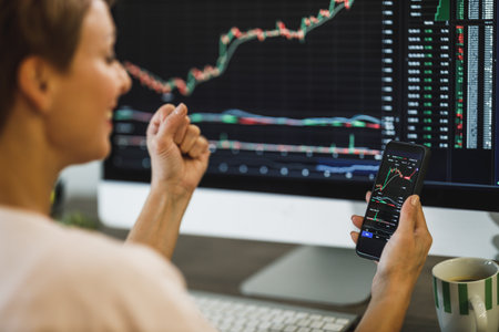 Middle age woman celebrating for success while trading with cryptocurrency on smartphone and...