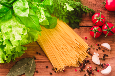 Cooking italian pasta spaghetti with cherry tomatoes, fresh green basil, salad and spices - top view on wood backgroundの写真素材