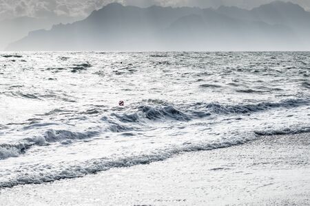 Milky sea waves and white shore with single ball on water and mountain silhouette