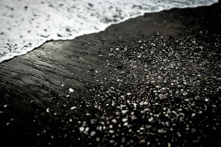 Sea foam wave on textured black sand beach with small stones. Black and white dramatic photo. Backgroundの写真素材